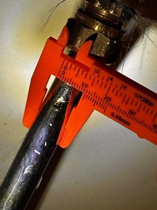 Röd skjutmått mäter metallrör som är anslutet till en gängad koppling med packningsmaterial.