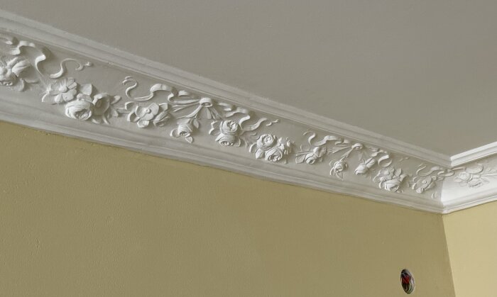 Dekorerad taklist med blommotiv i hörn mot beige vägg och vit takpanel, färdigställd efter renovering.
