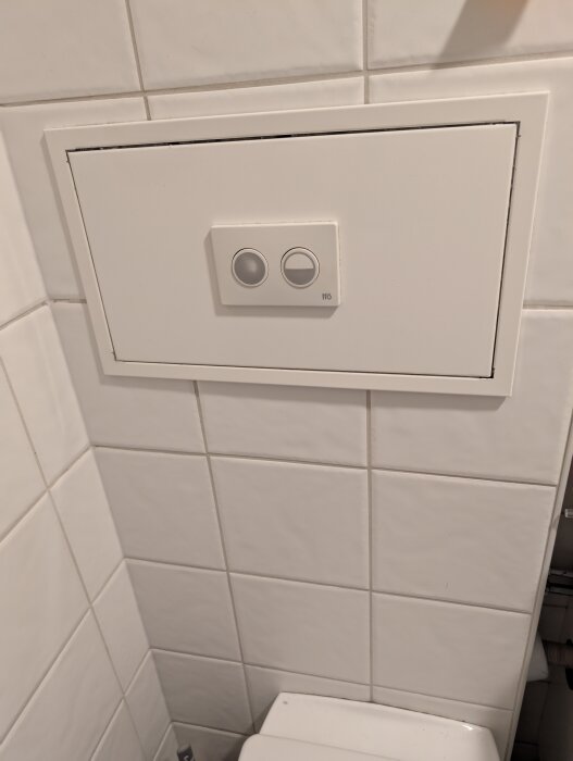 Väggmonterad spolknapp på toalett med två knappar och vit panel som användaren har problem med vid spolning.