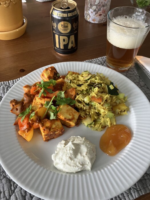 Paneer Tikka med grönsaksris, raita och mango chutney på tallrik, IPA-öl från Train Station Brewery i bakgrunden.