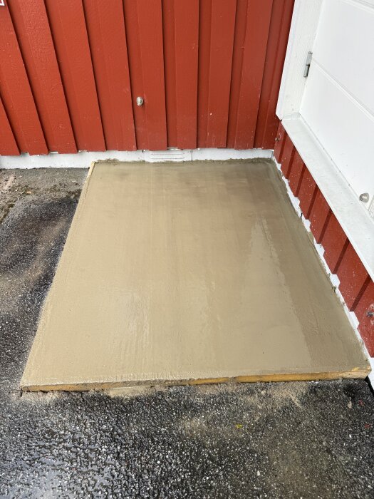 Nyss gjuten betongplatta vid röd trävägg, användande 15 säckar grovbetong.