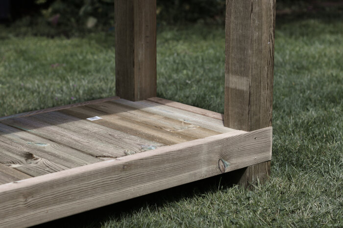 Trähylla monterad mellan två stolpar på ett utekök eller omplanteringsbänk under konstruktion i en trädgård.