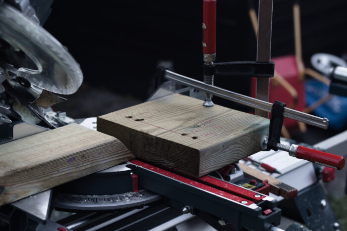 Träbit fastsatt i ett skruvstäd under arbete med kap- och gersåg. Fyra borrhål syns i träet.