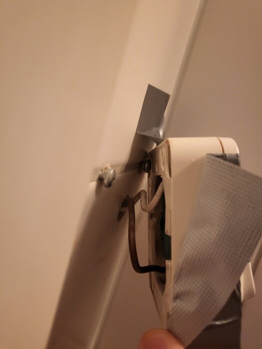 En lös elkontakt fastsatt med slangklämma och silvertejp på en vägg.