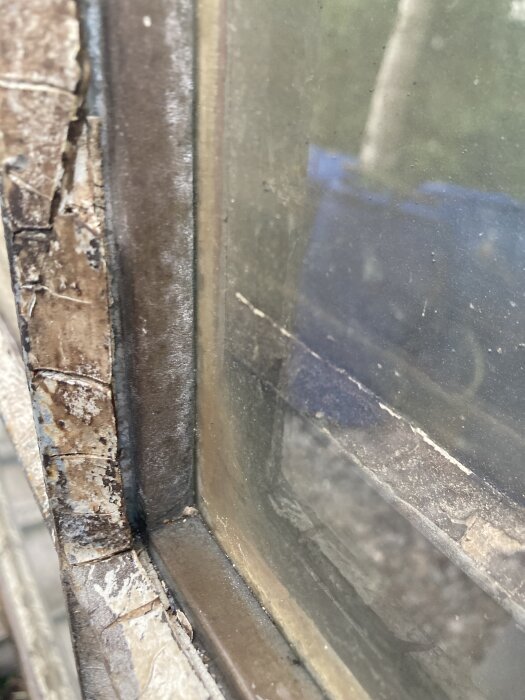 Närbild av gammalt och slitet fönster, där ramen visar tecken på avskavd färg och rost.