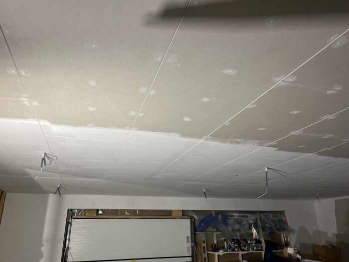 Tak under arbete med spackling och målning, flera hängande sladdar för belysning. En del av taket är vitmålat, resten är fortfarande spacklat.