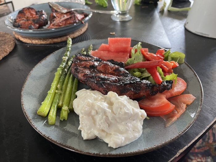 Grillad fläskkarré med potatissallad, vitlöksfrästa sparrisar, vattenmelon och sallad på tallrik.