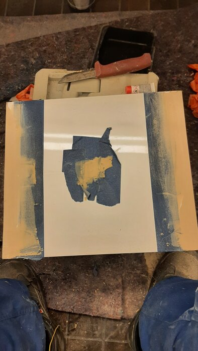 En vit dörr med blå maskeringstejp och kemiskt trä fyllning, omgiven av slipa- och putsmaterial. Verktyg synliga.