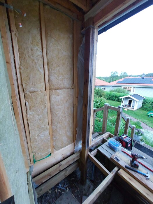 Byggarbetsplats med isolering i vägg, exponerade träreglar och en provisorisk gångbro. Verktyg och material syns på golvet.