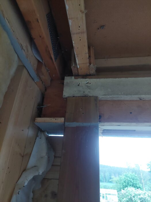 Trästolpe och reglar under renovering, synlig provisorisk konstruktion och en utomhusvy i bakgrunden.