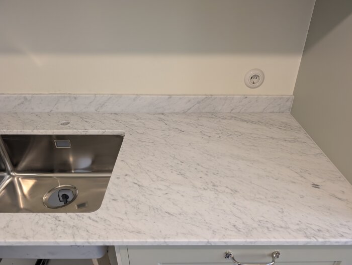Marmorbänkskiva i kök med rostfri diskho, installerad mot en ljus vägg med eluttag.