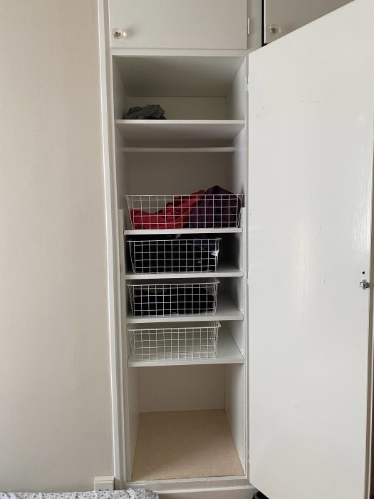 Vit garderob med öppna dörrar, hyllor och fyra trådkorgar fyllda med kläder.