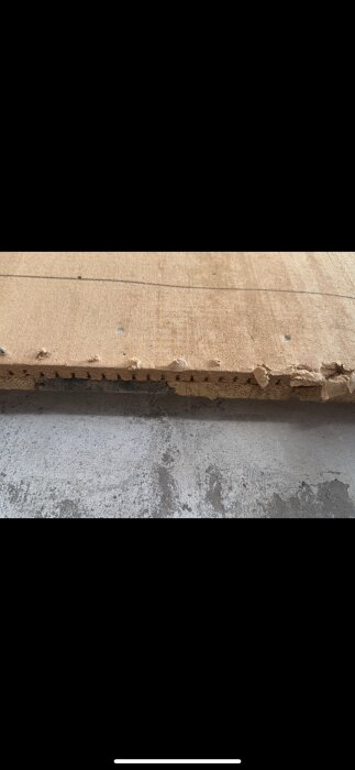 Närbild av en träskiva med ojämn kant och synliga lager eller skikt.