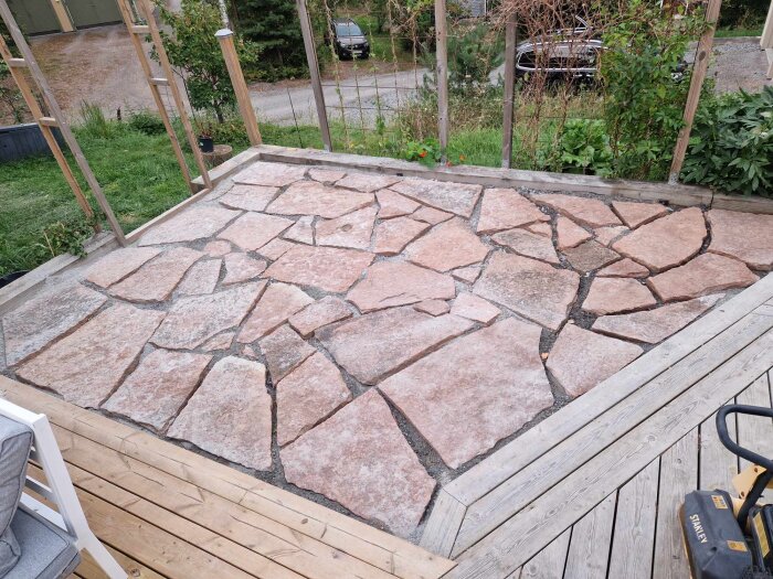 Naturstensplattor lagda på en uteplats, omringad av trästaket och grönska, innan sättsand har applicerats.