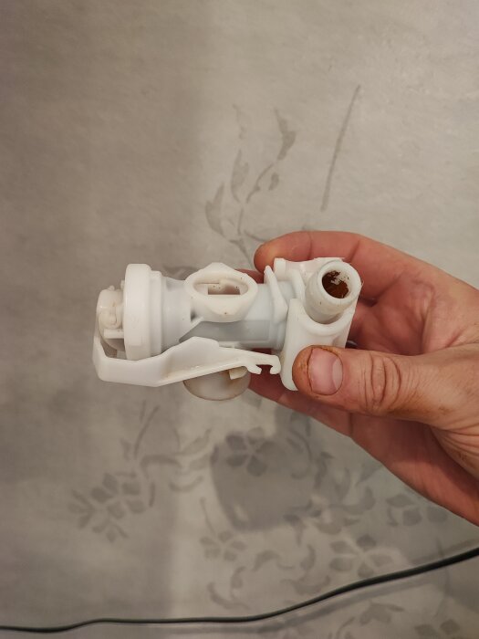 En hand håller en vit plastdel i ett rörsystem mot en ljus bakgrund, del av en diskussion om vattentrycksreglering.