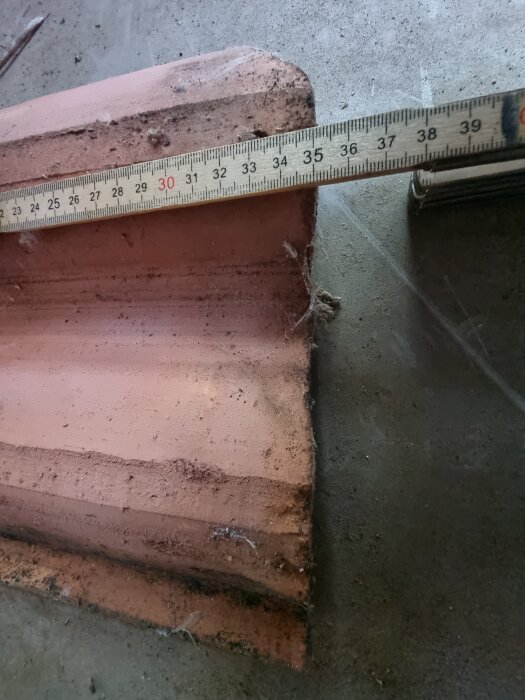 En tvåkupig tegelpanna med måttband som visar avstånd i centimeter på ovansidan.