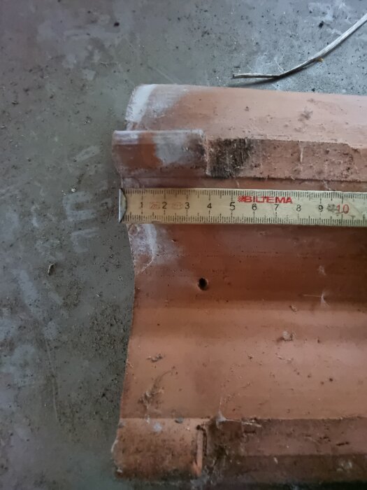 Gammal tvåkupig tegelpanna med måttband placerat över, visar cirka 21 cm i längd.