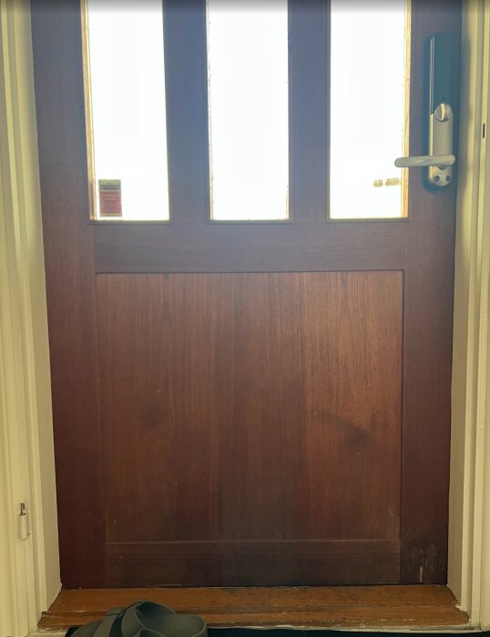 Träytterdörr med glaspartier och sprickor längst ned till höger i renoveringsprojekt. Dörrhandtag till höger.