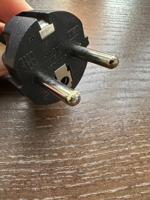Elkontakt med gulnad och något smält metall på pinnarna, visas i närbild på ett träbord.
