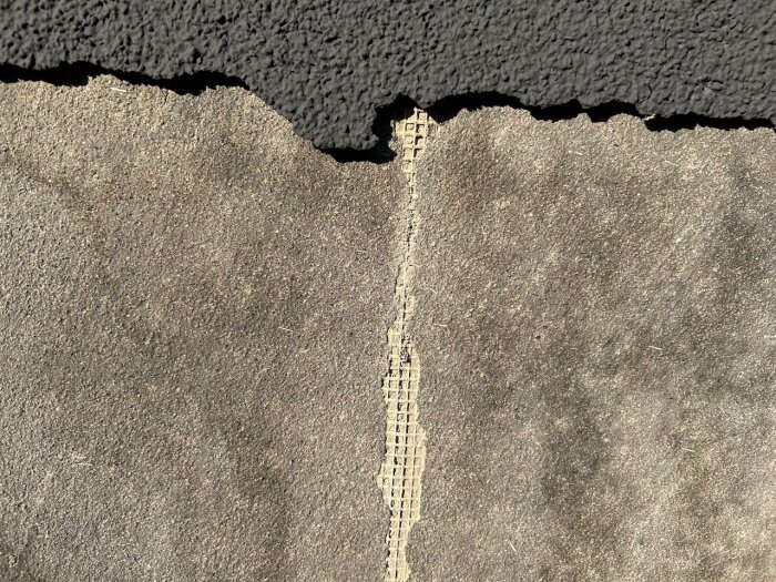 Fasad med skadad yta där färg flagnar, avslöjande glasfiberremsa under en tunn puts- eller spackelskikt.