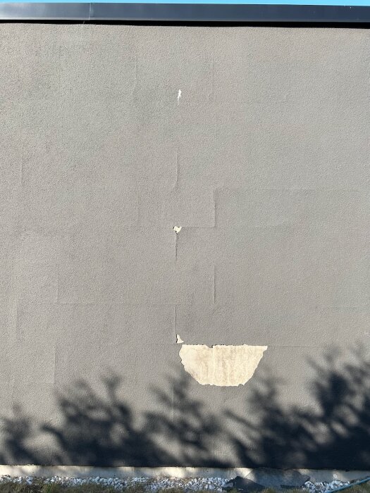 Fasad med släppt plastfärg, exponerar underliggande lager och skarvar med glasfiberremsa, i ett mönster som antyder cellplastblock.