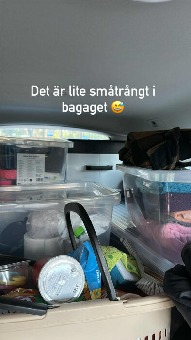 Bagageutrymme fullt med förvaringslådor och korgar, innehållande olika föremål. Text över bilden lyder: "Det är lite småtrångt i bagaget 😅".