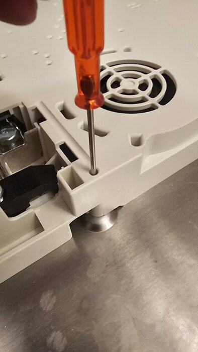 Skruvmejsel som sätts in i en skruv på ett hällhölje, bredvid en fläktliknande del av hällen.