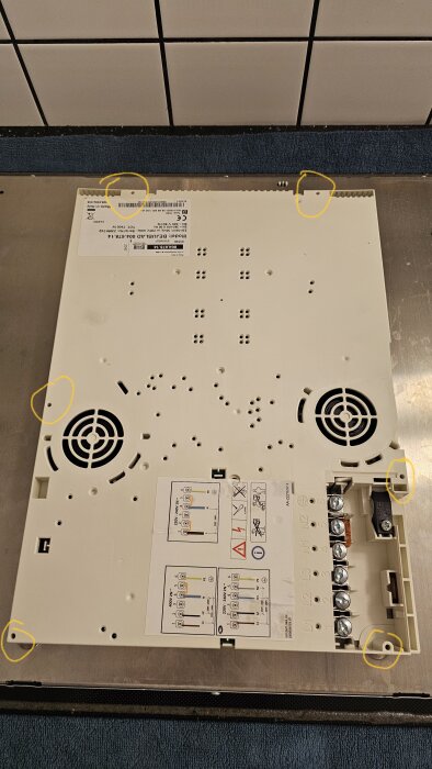 Baksida av ett elektrisk häll med märkliga skruvar inringade. Skruvarnas former gör det svårt att öppna kåpan. Plan för felsökning pågår.