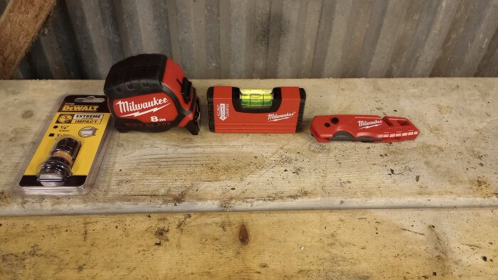 Verktyg på träbänk: Dewalt-bit, Milwaukee-måttband (8m), vattenpass och en kniv.