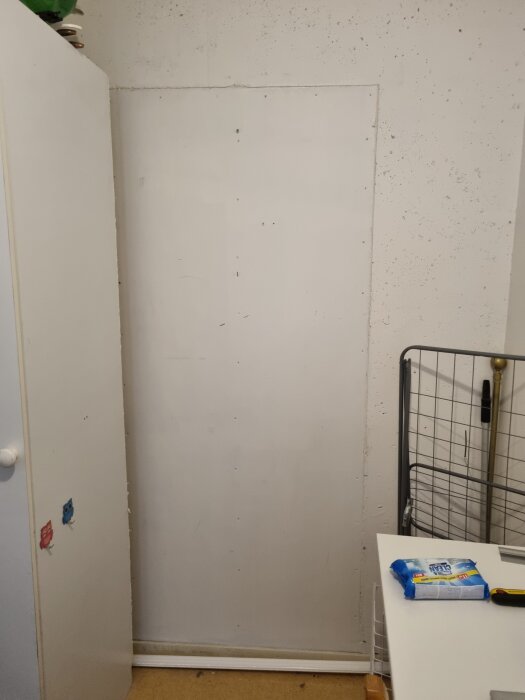 Ett förråd med en dörr som täckts över med gipsskiva, budgetlösning synlig bredvid ett skåp och arbetsbord med städmaterial.