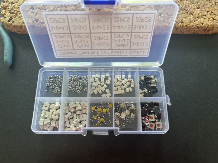 Plastlåda med olika typer av små knappar i fack, använd för reparation av en trasig laddare för bilbatteri.