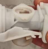 Vit inloppsventil med komplex form, visas hållen i handen.