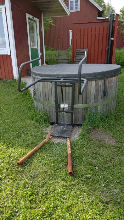 Badtunna med lockhållare, gräs och röd byggnad i bakgrunden.