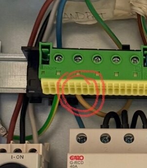 En brun ledare är inkopplad i en elcentral med gröna och gula anslutningar, eventuell skyddsjord markerad med röd cirkel.