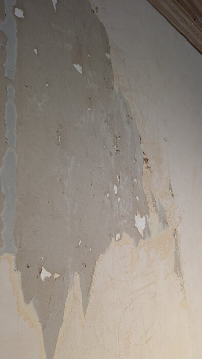 Borttagna tapeter som har slitit upp ytterlagret av en gipsskiva, vilket skapar skador på väggen.