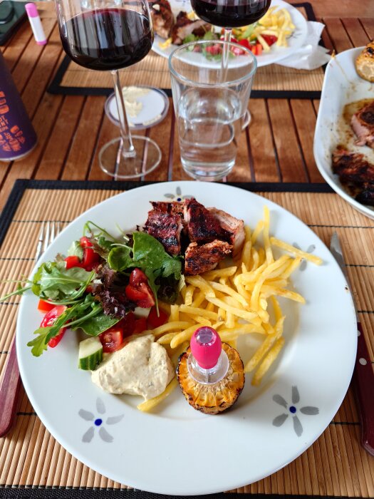 Tallrik med flintastek, pommes frites, sallad och sås. Två vinglas och ett glas vatten på bord av trä.