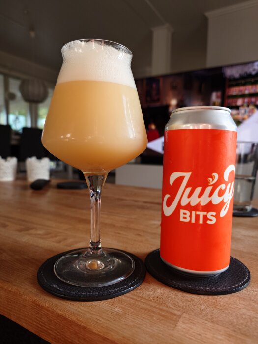 Glas med ljus öl och en burk 'Juicy Bits' på ett bord.