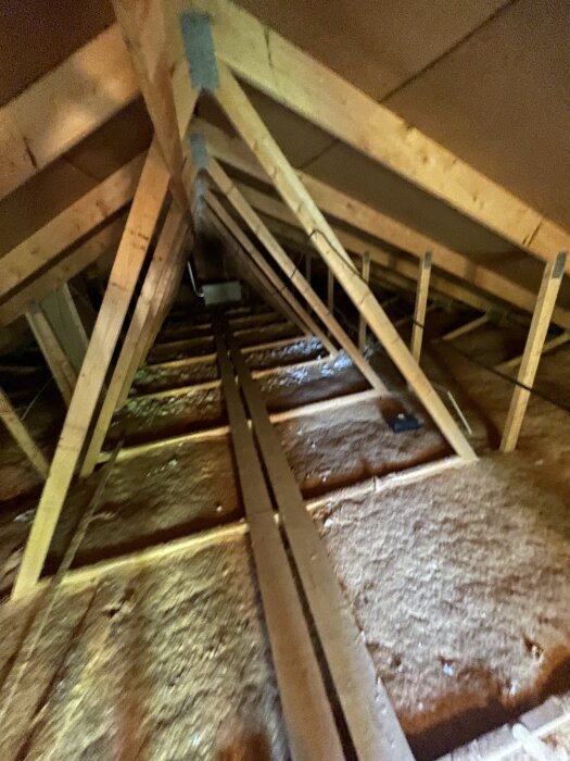 Självbärande takstolar på en oinredd vind med isolering och trädetaljer.