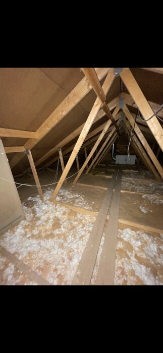 Självbärande takstolar i en vind med synlig isolering och träbalkar.