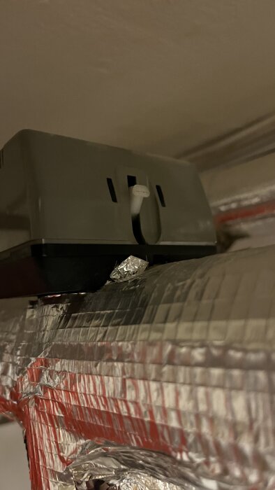 En vit spak på en grå enhet ovanpå ett isolerat rör. Spaken är i upprätt läge och kan inte tryckas ner.