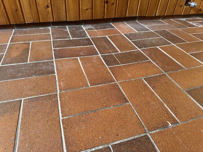 Golvet med brunt klinker i olika nyanser visar sprickor och ojämnheter.