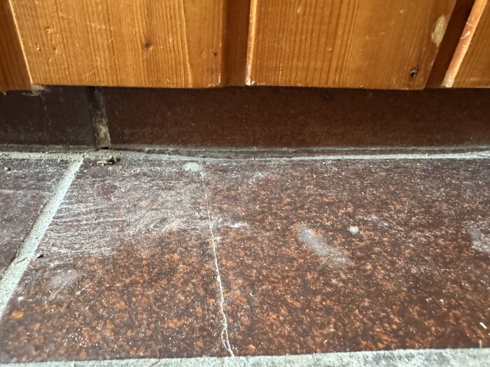 Skadat brunrött klinkergolv med tydliga sprickor vid kant mot träpanel i ett äldre badrum.