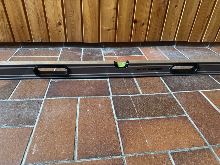 Vattenpass på ojämnt klinkergolv med synliga sprickor och höjdskillnader, del av renoveringsdiskussion för badrumsgolv från 1975.