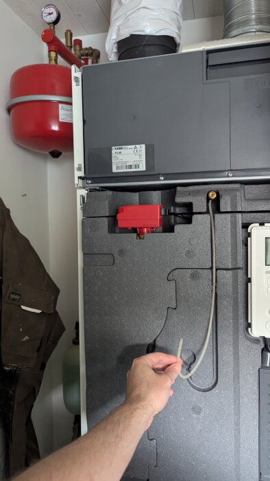 En värmepump i närbild med en hand som håller ett ventilsystem i ett försök att lufta systemet. En röd expansionstank syns i bakgrunden.