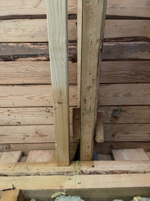 Ojämna takstolar och träbalk med grön tråd visar lutning vid renovering av sommarstuga.