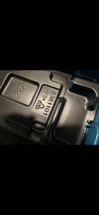 Närbild av en plastfodral med märkning "8381101 >PS<" och återvinningstriangel.