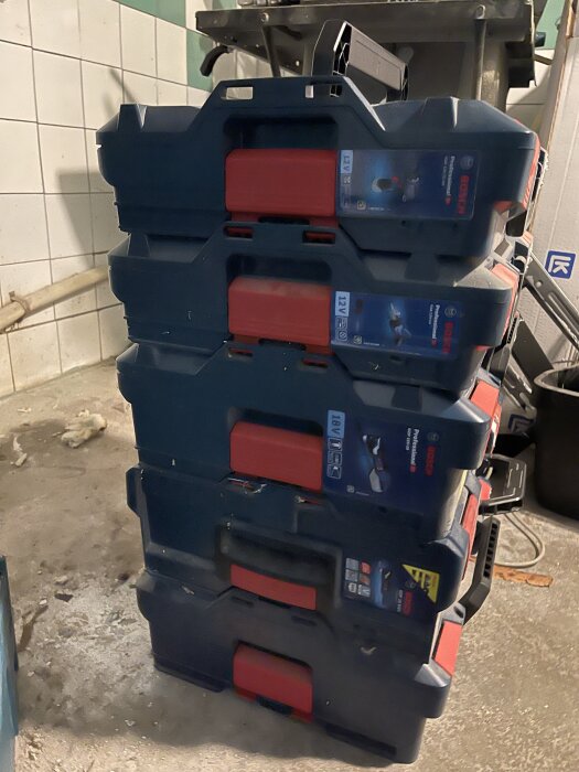 Fyra staplade Bosch L-Boxx väskor i ett garage, förvaringslösningar för verktyg, stående på ett smutsigt golv.