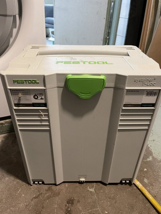 Bild på en grå Festool systainer T-Loc med grönt handtag, stående på ett golv.