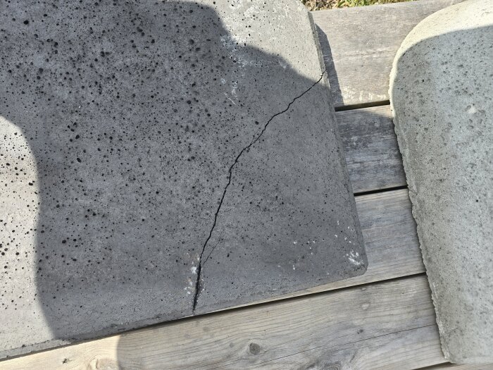 Sprucken platta i betong med tydlig spricka liggande på trädplankor, relaterad till en murad grill från Bauhaus.