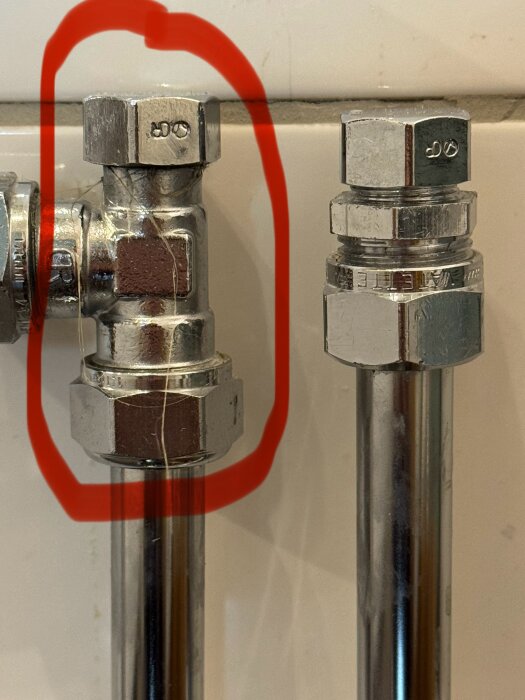 Två rörkopplingar, vänster är konisk med täcklock och markerad i röd cirkel, höger är plan koppling. Finns framför vit kakelvägg.